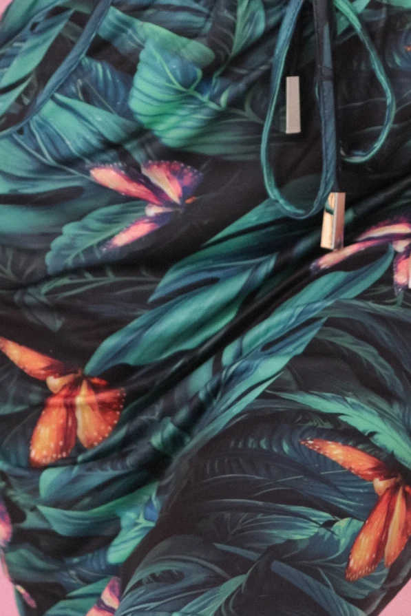 Modelka prezentuje sportową sukienkę z tropikalnym nadrukiem 3D w liście i motyle, z dekoltem typu łódka i kieszeniami, marki Numoco. Stylowa propozycja na lato – modna, wygodna i wyprodukowana w Polsce.