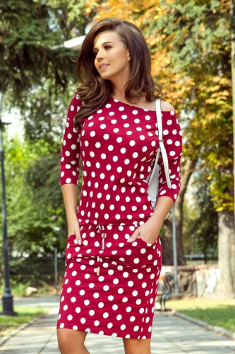 Rochia sport elegantă este de culoare roșie cu buline albe, având mâneci trei sferturi și un cordon în talie. Materialul lejer și designul cu buzunare o fac ideală pentru un look casual și confortabil.}
