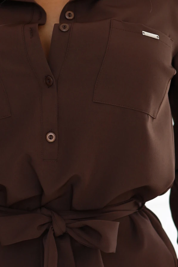 Modelka prezentuje elegancką koszulową sukienkę typu szmizjerka w kolorze czekoladowym, z kołnierzykiem, guzikami i wiązaniem w talii; produkt polski marki Numoco, idealny na co dzień i do pracy.