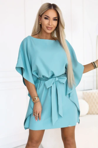 Modelul poartă o rochie mini turcoaz Numoco cu mâneci tip liliac și cordon legat la talie.}