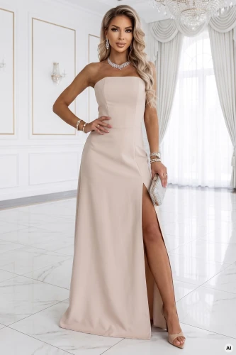 Modelul prezintă o rochie maxi Numoco bej deschis fără bretele cu șlit înalt - o elegantă rochie de seară într-un interior minimalist.}