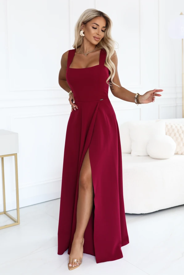 Model într-o rochie maxi bordo elegantă Numoco cu decolteu pătrat, bretele late, talie accentuată și șliț înalt la picior, prezentată într-un interior luminos și modern.