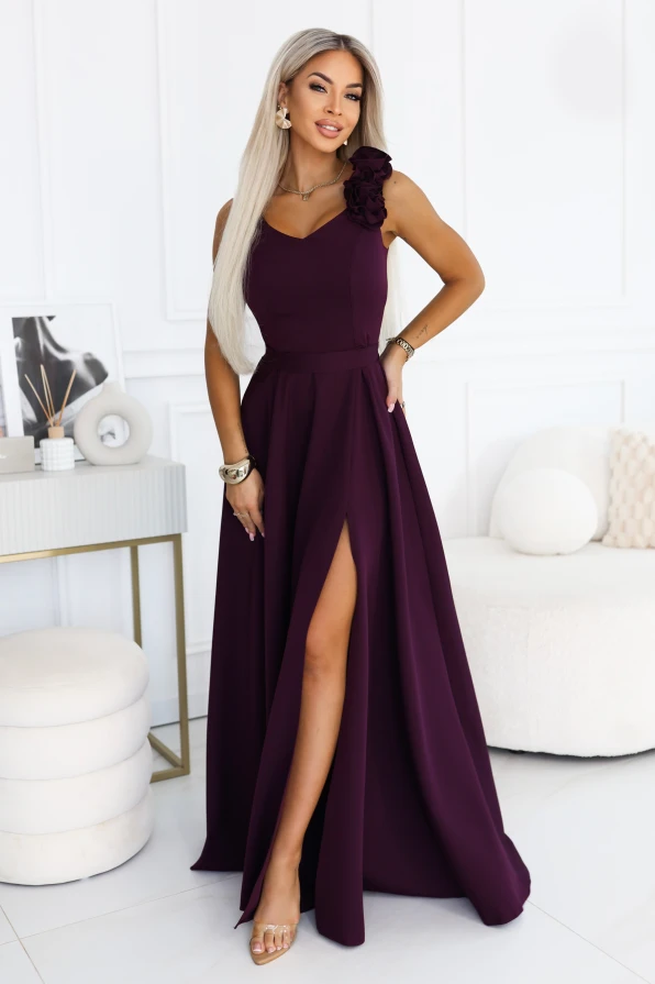 Model purtând o rochie maxi Numoco în culoarea prunei coapte, cu decolteu în V, trandafiri decorativi pe umăr, talie evidențiată și parte de jos evazată cu despicătură înaltă la picior.