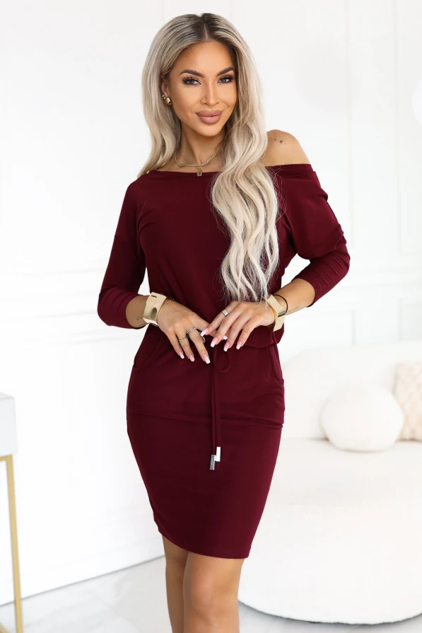 Model purtând o rochie sport bordo Numoco chiar deasupra genunchilor, cu decolteu barcă ce dezvăluie un umăr, mâneci 3/4, buzunare laterale și legătură la talie.