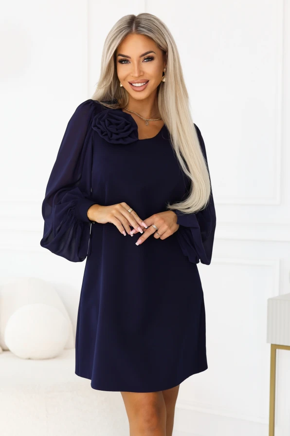 Model purtând rochia bleumarin NELIA de la Numoco, cu croi trapez chiar deasupra genunchilor, trandafir decorativ la decolteu și mâneci lungi, transparente, terminate cu manșete late cu nasture.