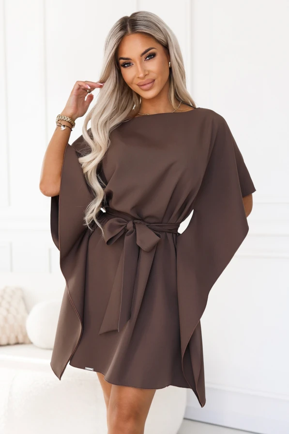Model purtând rochia SOFIA de la Numoco în nuanța maro mocha. Rochia ajunge chiar deasupra genunchilor, are decolteu barcă, mâneci late de tip fluture și o curea legată la talie în fundă.