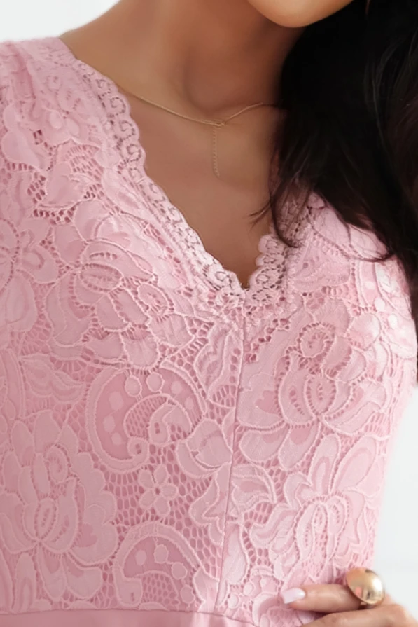 Modelka prezentuje różową, koronkową sukienkę z asymetrycznym dołem marki Numoco – elegancką propozycję na wesele lub inne uroczystości, wykonaną w Polsce.