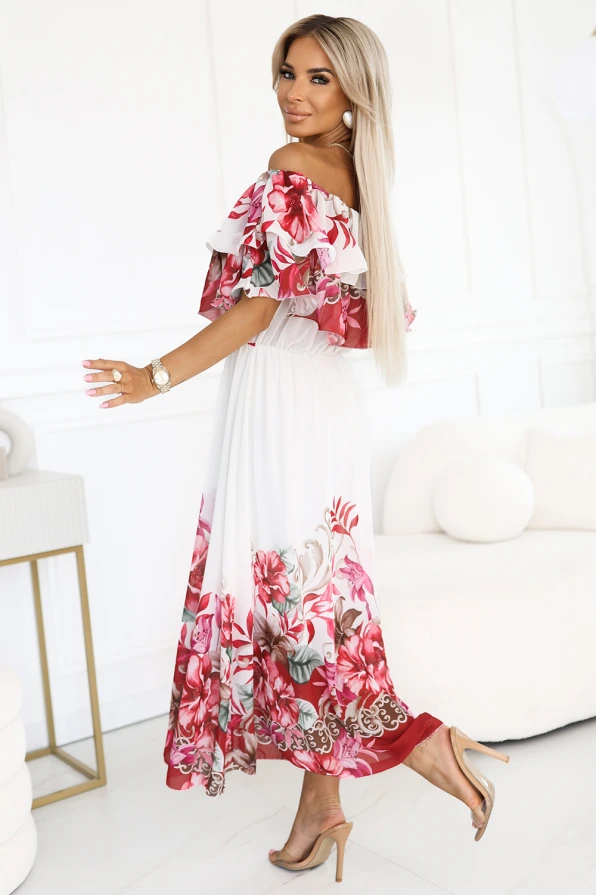 Modelka z gracją prezentuje letnią sukienkę maxi hiszpankę z falbaną i kwiatowym wzorem w odcieniach czerwieni i różu. Jej swobodna poza i uśmiech podkreślają romantyczny, kobiecy charakter tej stylizacji od Numoco Basic.
